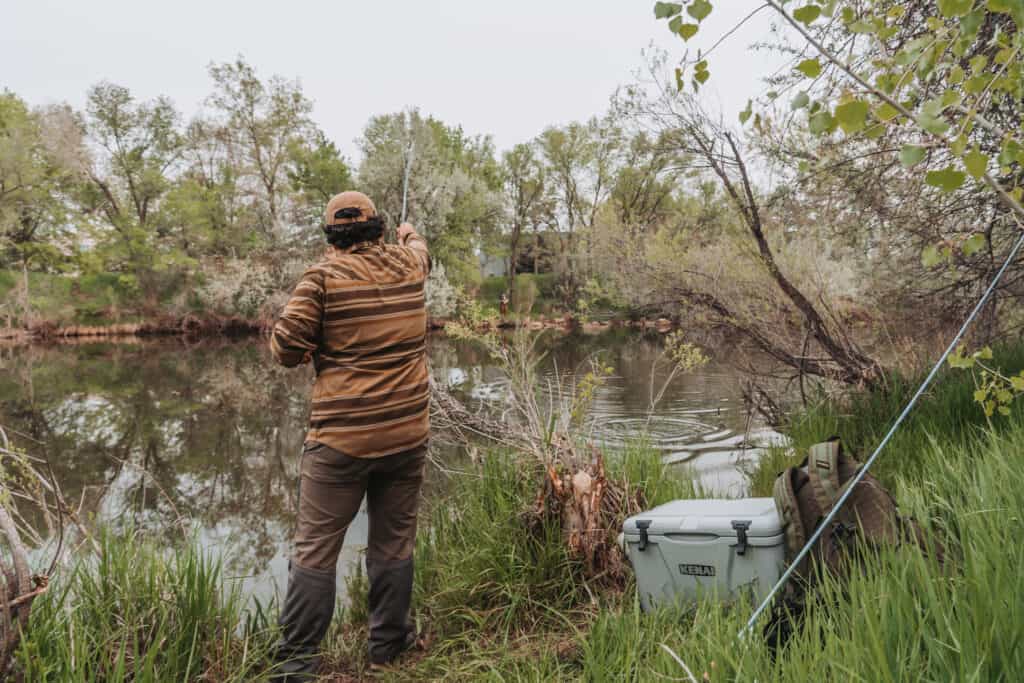 man casting into stream with Kenai Cooler sitting on bank