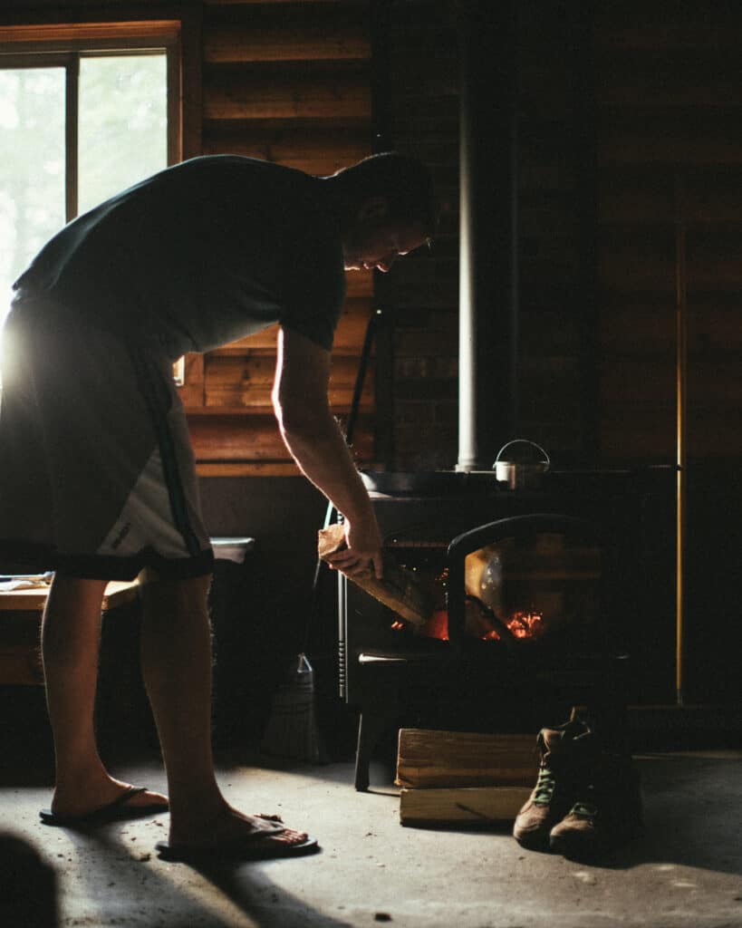 man stoking a woodstove with cast iron skillet ontop of woodstove