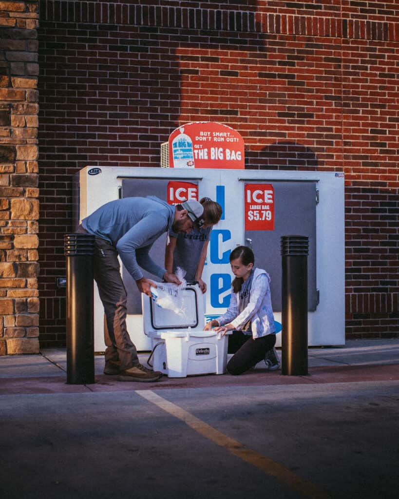 man and women filling ice in a grizzly cooler outside a ice cooler