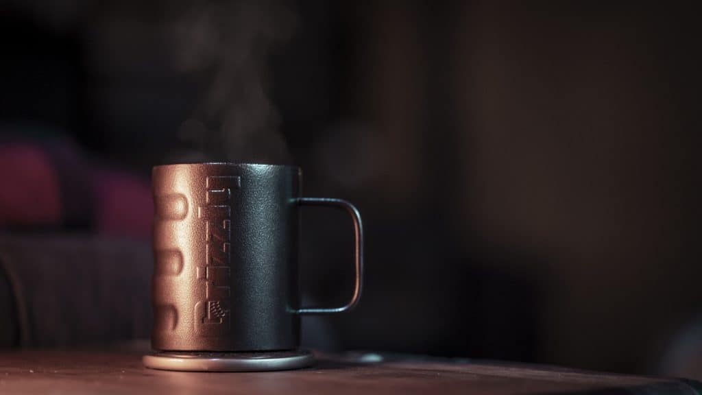 grizzly grip camp cup in textured copper finish sitting on table with steam coming out of coffee cup