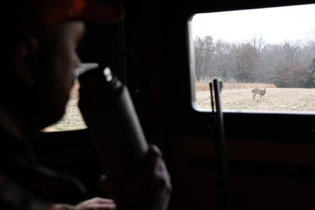 Hunter sitting inside hunting blinds looking at a nearby deer