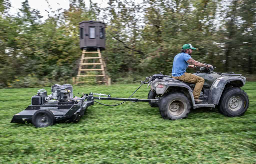 hunting blind on elevated stand in background, with man on 4 wheeler in foreground. 