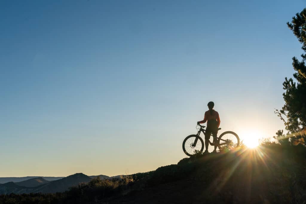 silhouette of a women and mountain bike on a ridge just as the sun is cresting the ridge at dawn
