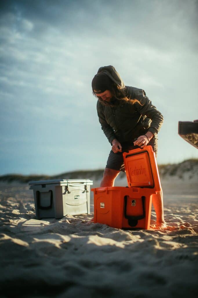 man opening a grizzly cooler at music festival on beach
