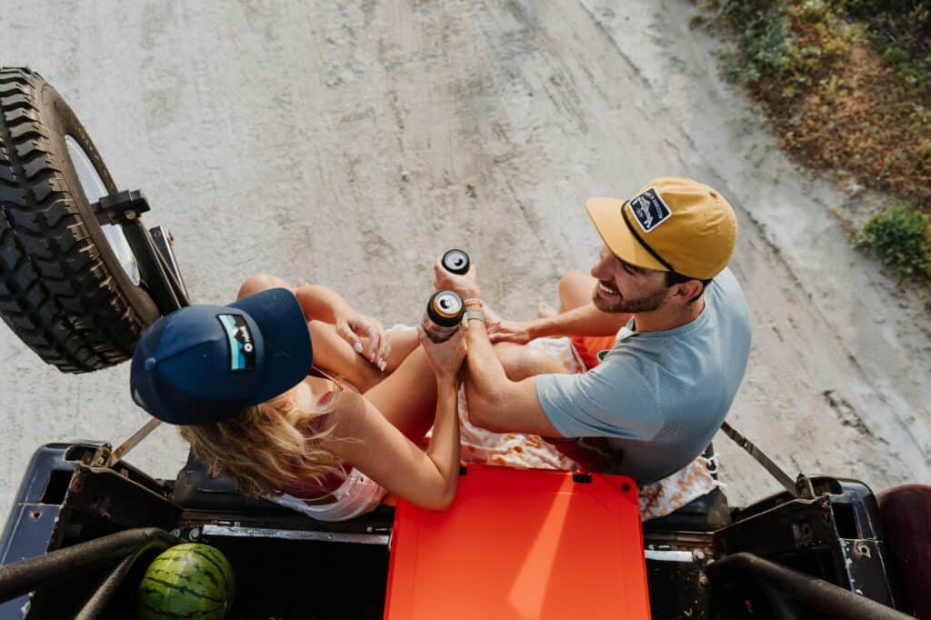 2 people sitting on tailgate at summer palooza enjoying refreshments while using grizzly coolers drinkware, overhead angled shot