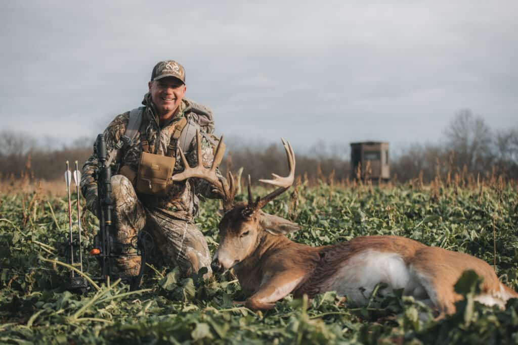 hunter with buck, in food plot with hunting blind in background