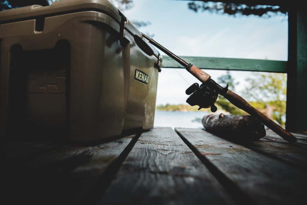 topwater bass fishing gear, resting on a Kenai cooler on dock. Lake in background.