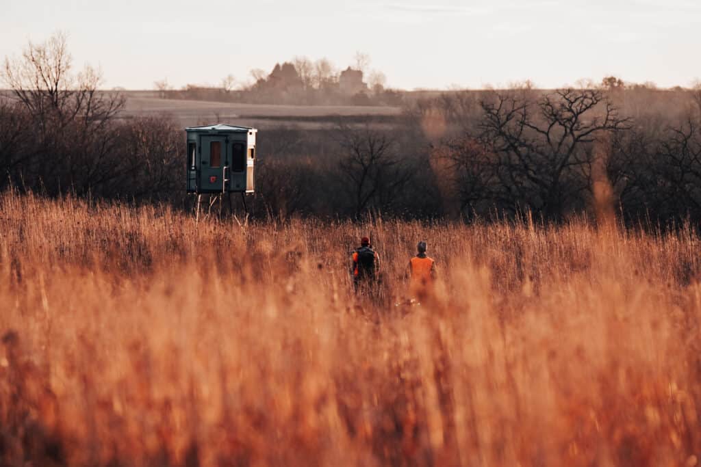 women hunting walking through tall hay field into the sunrise